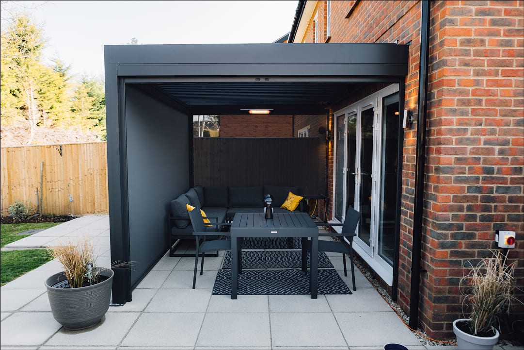 Aluminium louvred pergola over a UK garden patio, adjustable slats half-open on a grey overcast afternoon, showing year-round use