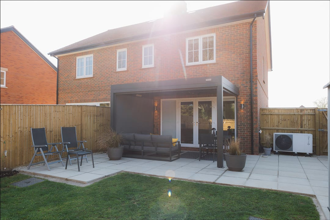 Aluminium bioclimatic pergola with louvres half-open over a UK garden patio on a grey autumn afternoon, rain visible in background