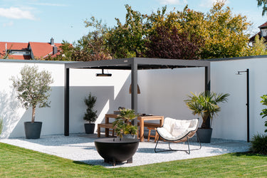 Outdoor patio area with a pergola, table, chairs, and decorative plants on a sunny day.