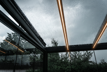 Conservatory glass roof with raindrops and interior lights reflecting on a rainy day