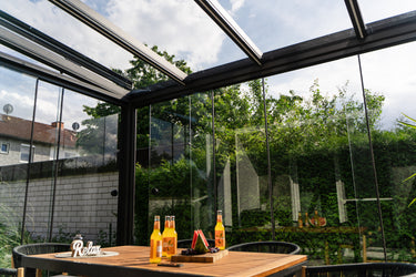 Glass-walled conservatory with outdoor view, table with drinks and snacks.
