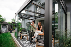 Two people sitting in a modern conservatory with chairs and a table.