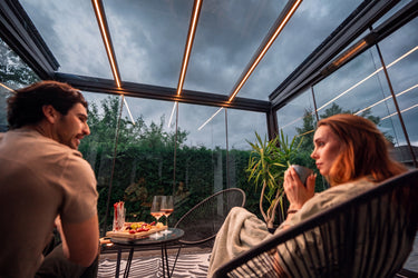Two people sitting in a modern conserratory space with a view of trees.