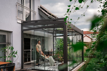 Two people in a conservatory living space with greenery around.